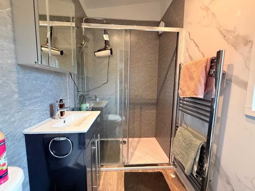 Moderne badkamer met douchecabine, wastafel met opberglade en handdoekenrek aan de muur.