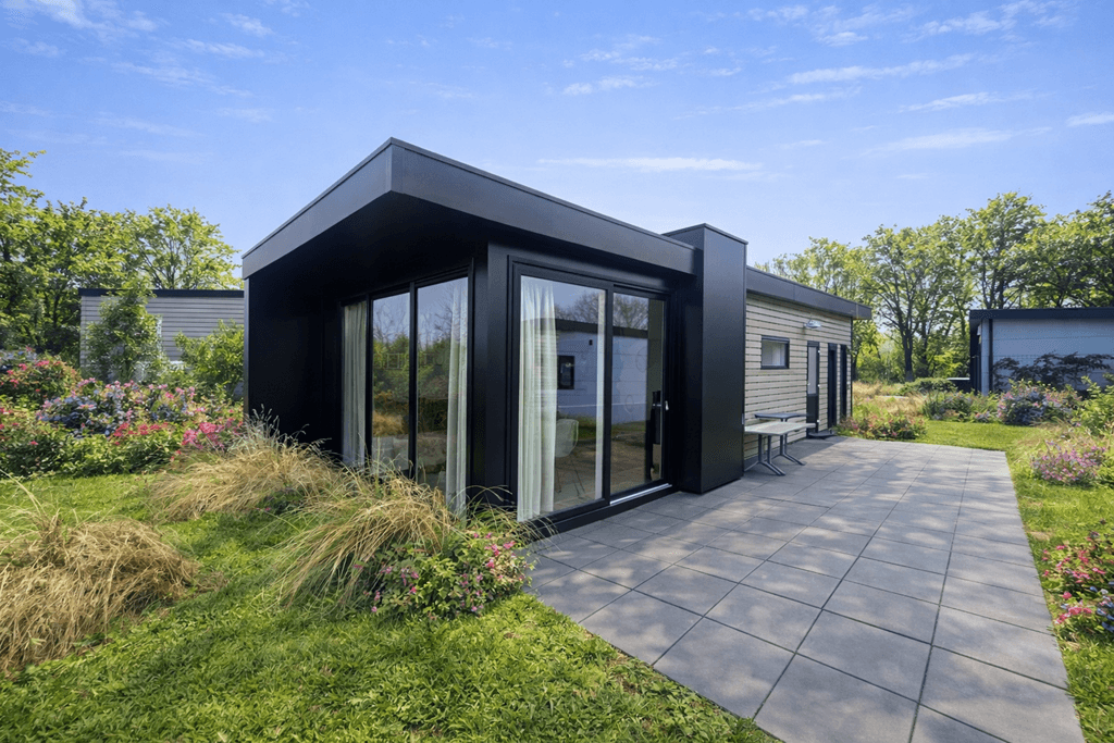 Moderne vakantiewoning met grote glazen schuifdeuren, omgeven door een groene tuin en betegeld terras