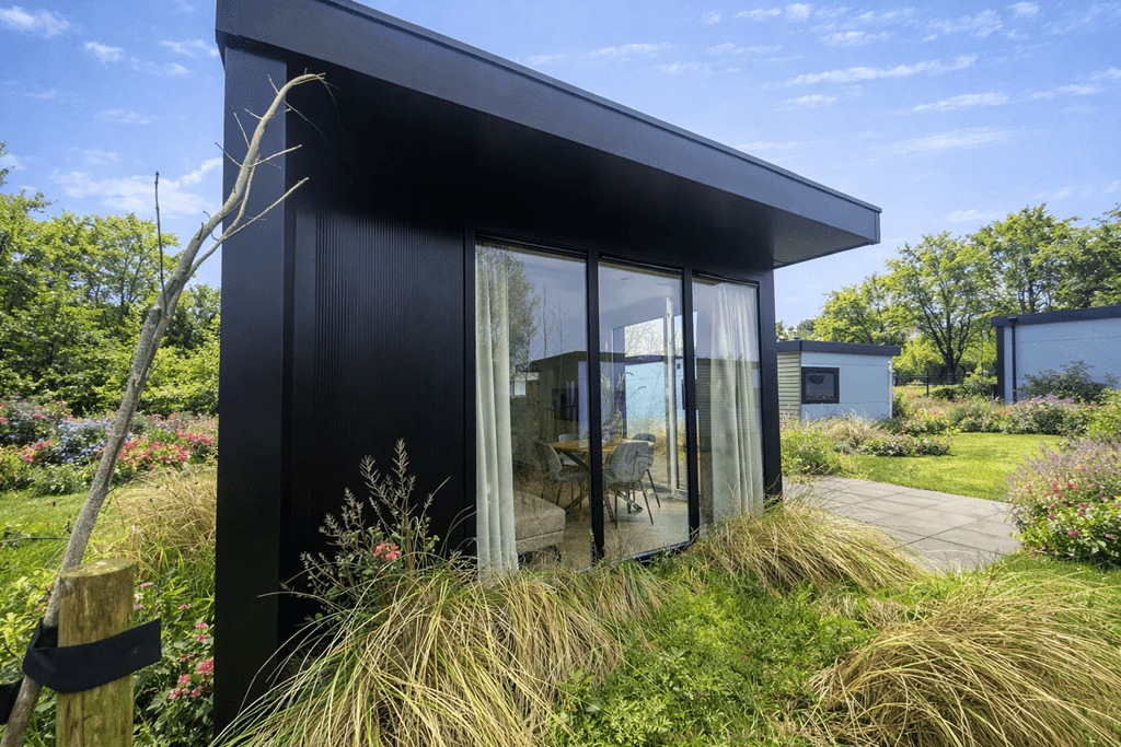 Moderne vakantiewoning met grote ramen, omgeven door groen en kleurrijke bloemen, gelegen op EuroParcs Texel.