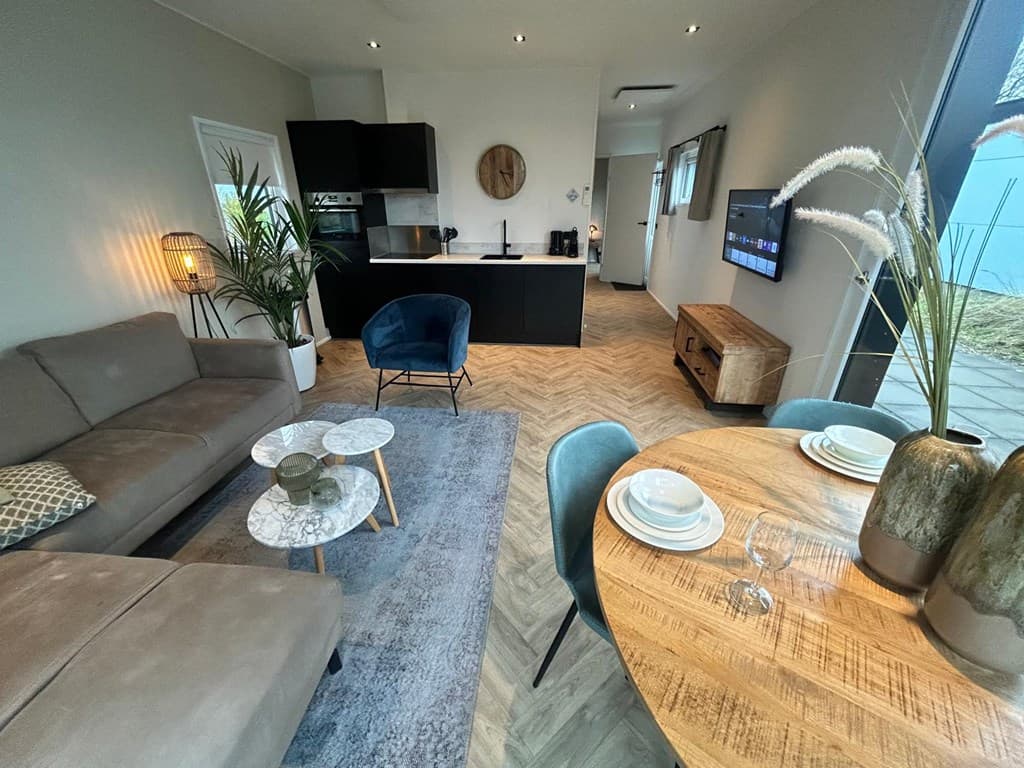 Moderne woonkamer met zithoek, eettafel, kitchenette en grote ramen voor naturel lichtinval.