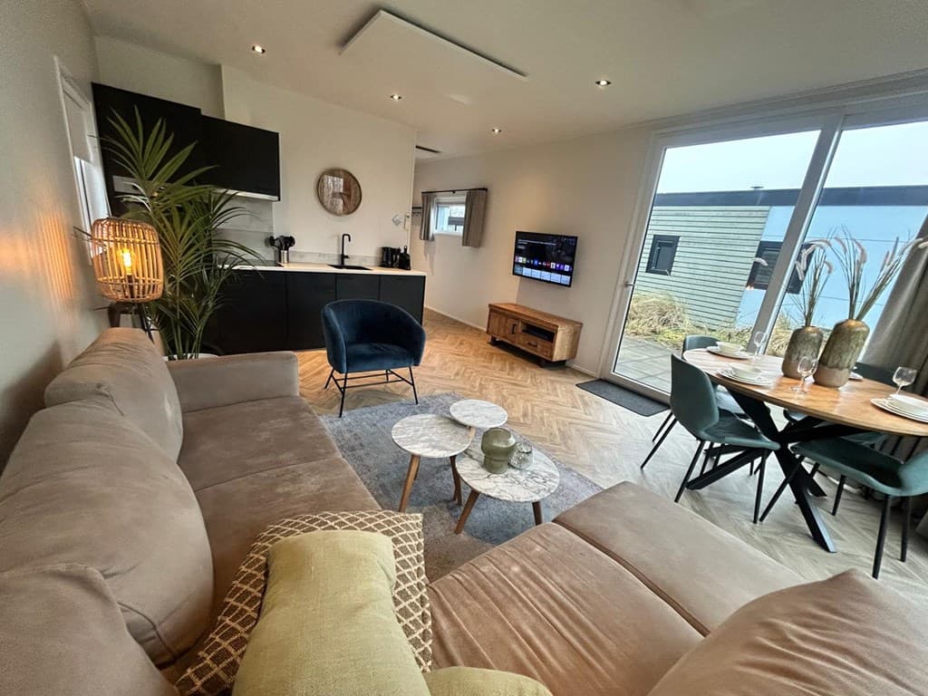 Woonkamer met bank, eettafel en keuken in een moderne inrichting met uitzicht op buitenruimte