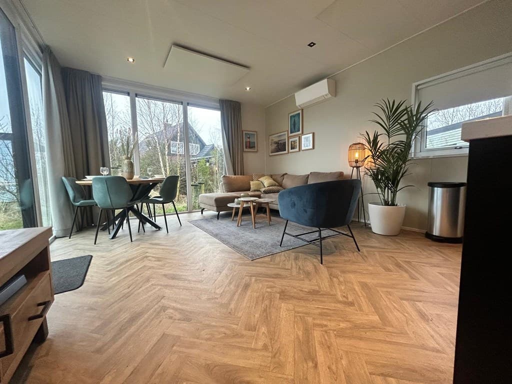 Moderne woonkamer met grote ramen, zithoek, eettafel en planten, licht en minimaal ingericht.