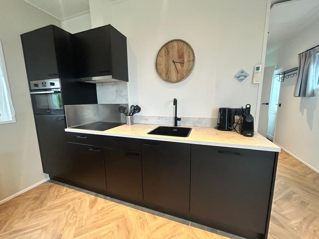 Moderne zwarte keuken met werkblad, een oven, kookplaat, gootsteen en wandklok in lichte interieurtint.