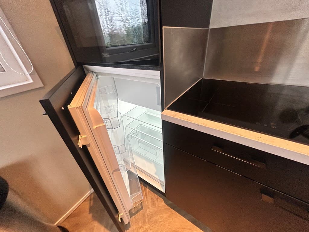 Ingebouwde koelkast in een moderne keuken met glazen planken en een inductiekookplaat zichtbaar.