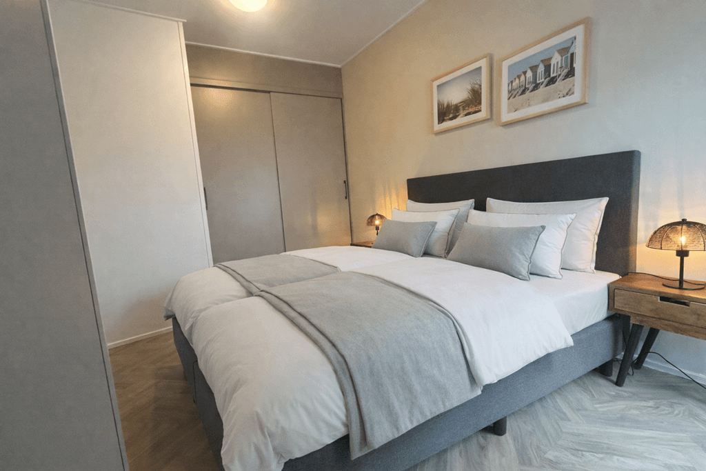 Sfeervolle slaapkamer met twee eenpersoonsbedden, nachtkastjes en fotos aan de muur.