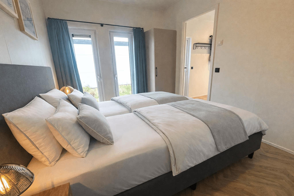 Slaapkamer met twee eenpersoonsbedden, nachtkastjes en openslaande deuren naar buiten.