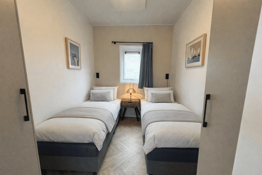 Slaapkamer met twee eenpersoonsbedden, nachtkastje en raam met gordijnen. Verfijnde decoratie aan de muur.