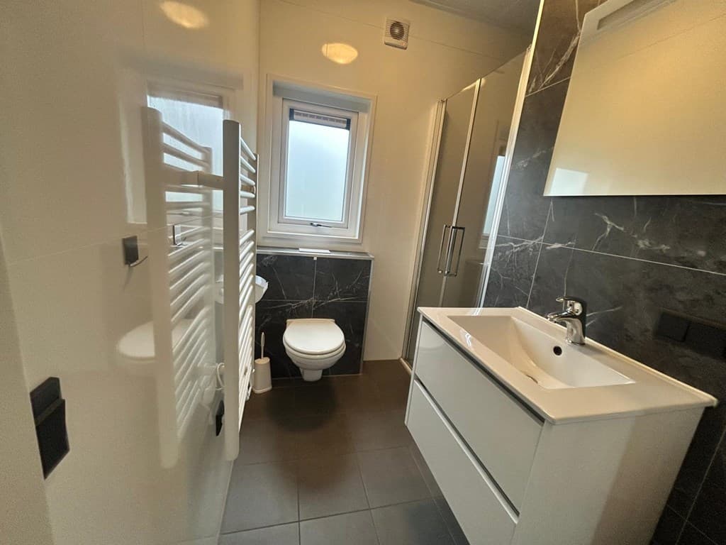 Moderne badkamer met een inloopdouche, toilet, wastafel en handdoekenradiator in een lichte inrichting