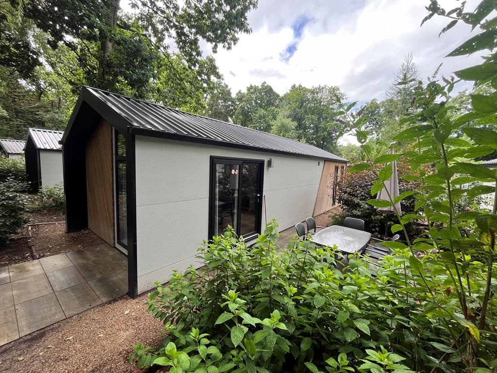 Moderne vakantiewoning met een terras en tuin, omringd door bomen en groen.