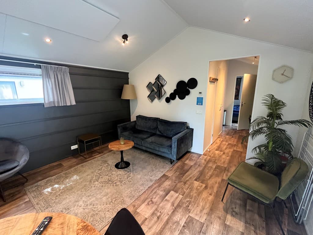 Woonkamer met een bank, een tafeltje, decoratieve wandobjecten en een plant, aansluiting naar andere ruimtes zichtbaar.