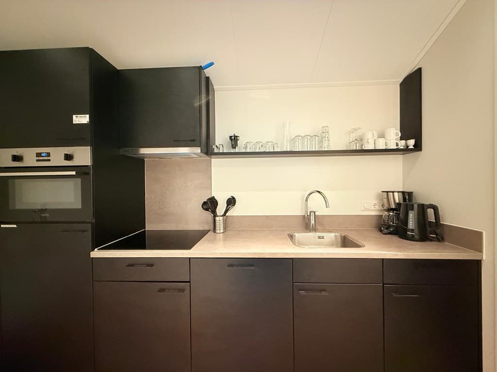 Moderne keuken met donker houten kasten, spoelbak, kookplaat en glazen servies op een open plank.