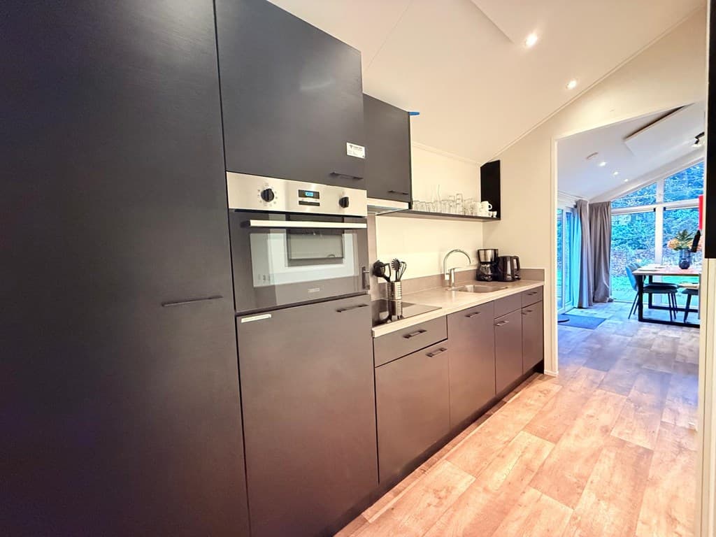 Moderne keuken met zwarte kasten, oven, kookplaat en uitzicht op eetgedeelte met veel lichtinval.