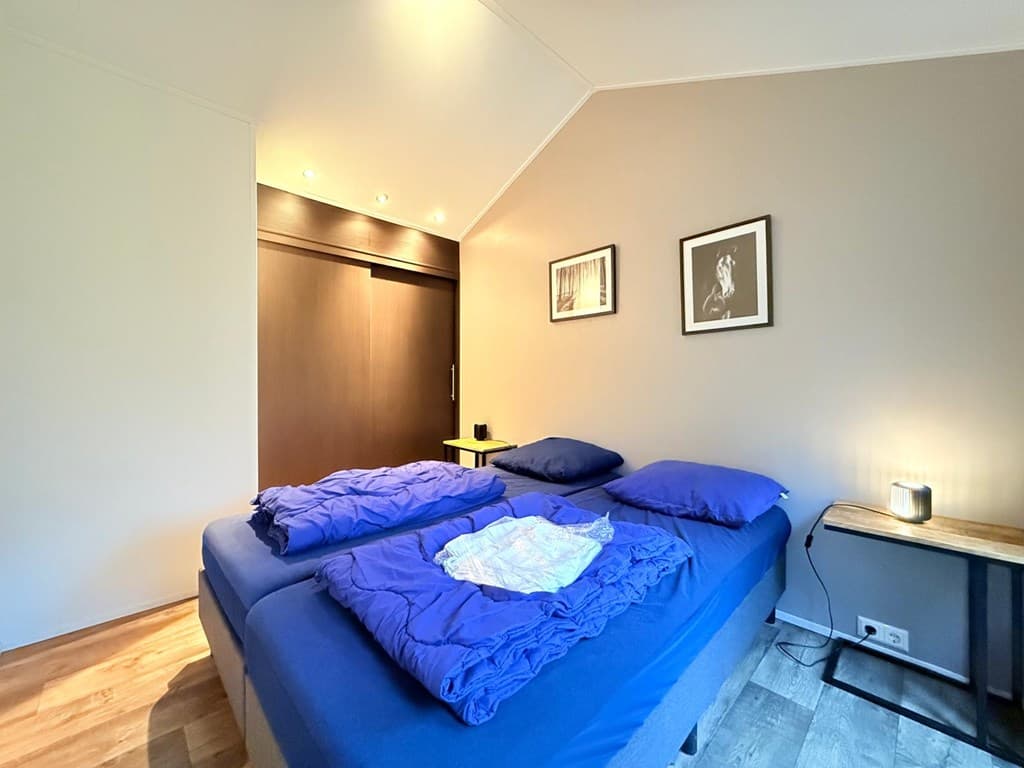 Slaapkamer met twee aparte bedden, houten vloer en enkele foto's aan de muur. Verlichting aan het plafond en een nachttafel n