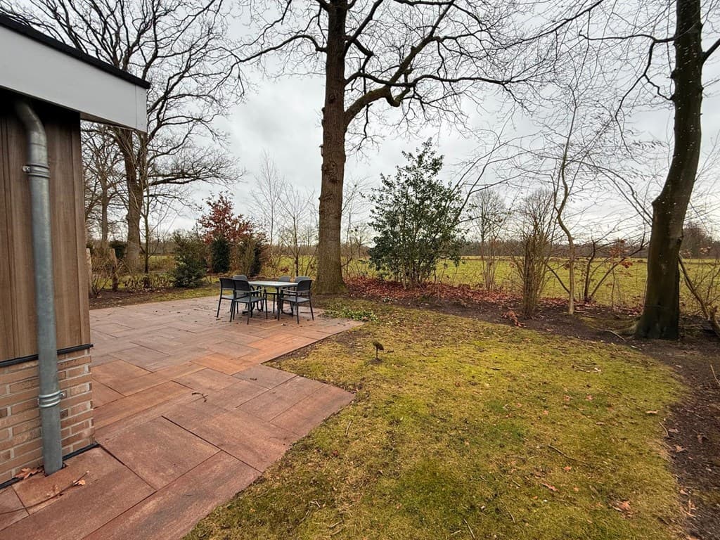 Terras met tuintafel en stoelen, omgeven door gras en bomen, met uitzicht op een open veld