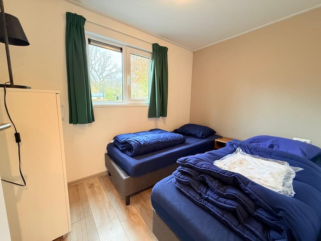 Slaapkamer met twee eenpersoonsbedden, groene gordijnen en een kast in een lichte ruimte met houten vloer.