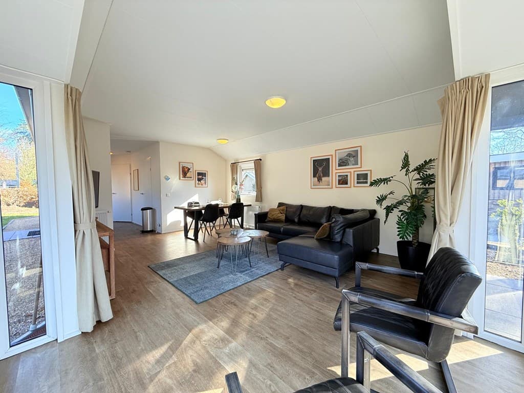 Moderne woonkamer met een bank, fauteuils, kunst aan de muur en grote ramen voor natuurlijk licht.