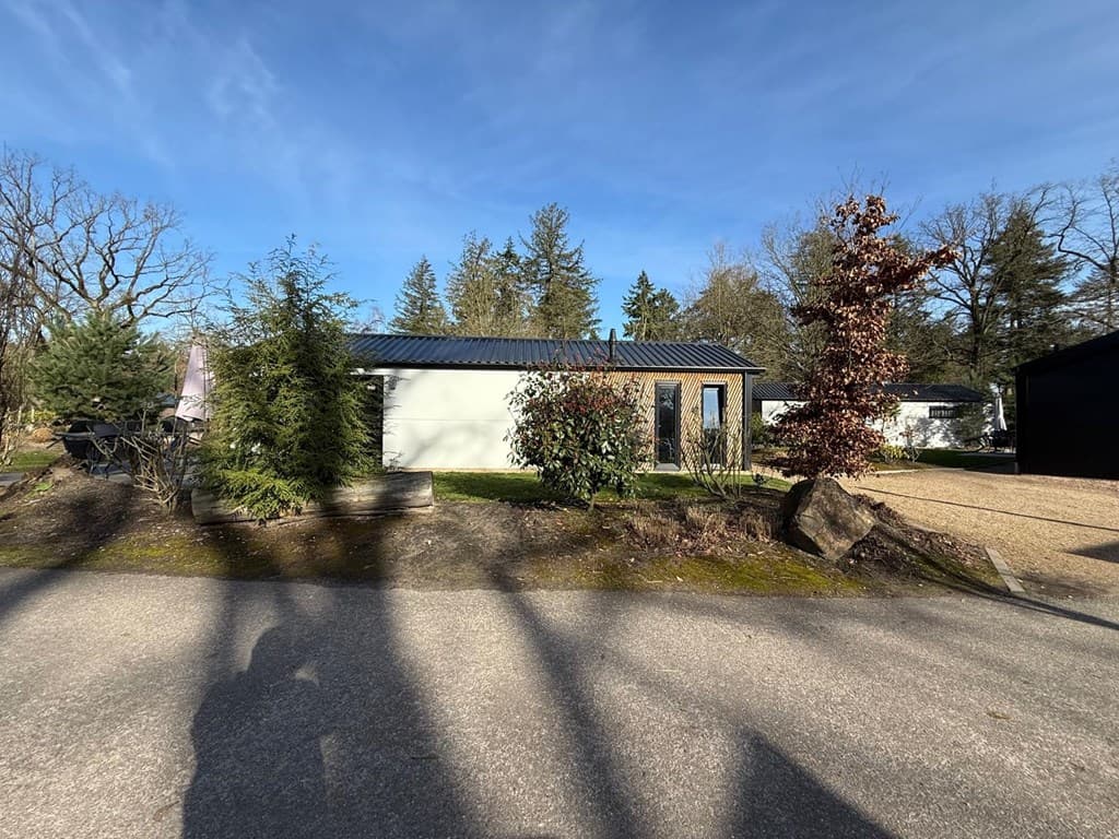 Moderne vakantiewoning met groene tuin en omliggende bomen, gelegen aan een parkeerplaats in EuroParcs Resort De Utrechtse He
