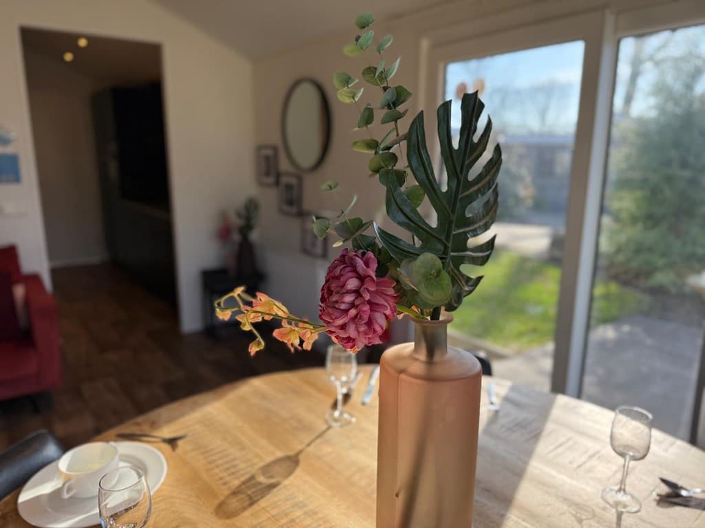 Tafellaken met houten tafel, een vaas met bloemen en een uitzicht op de tuin door grote glazen deuren.