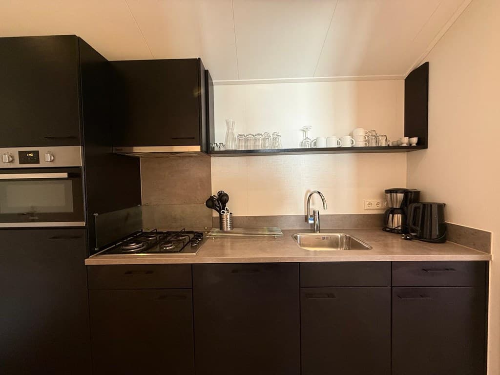 Moderne keuken met zwarte kasten, gasfornuis, spoelbak en gemêleerd werkblad met glazen en servies erop.