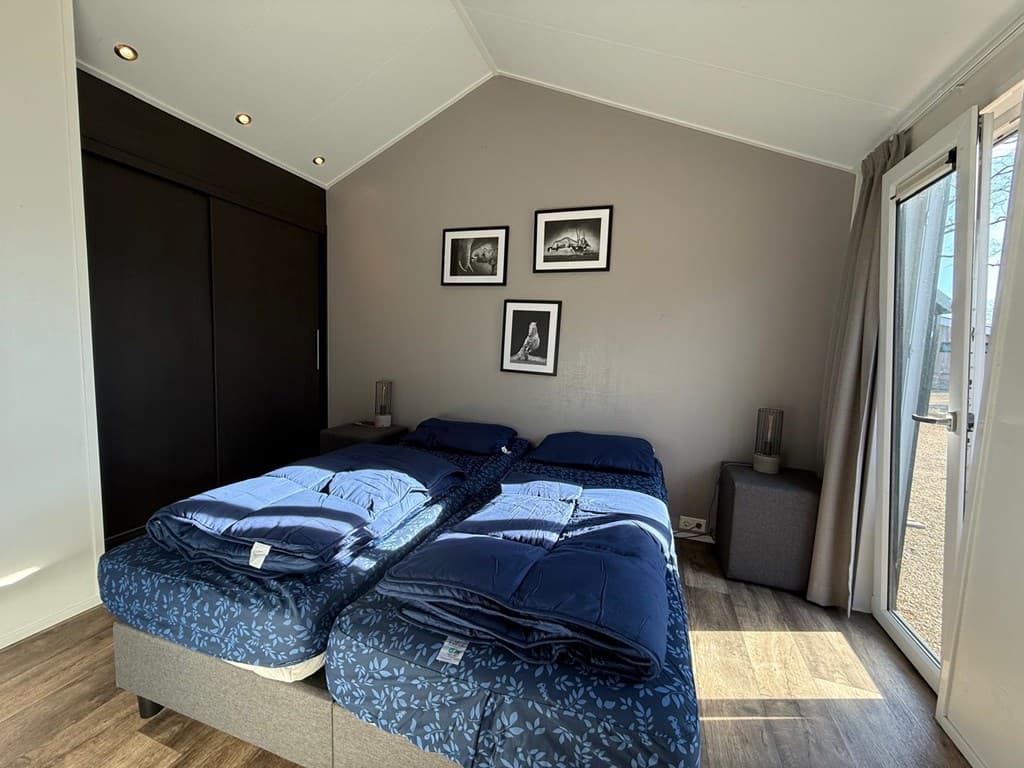 Slaapkamer met twee aparte bedden, donkere kastenwand en enkele wanddecoraties, toegang tot buiten via een schuifdeur.