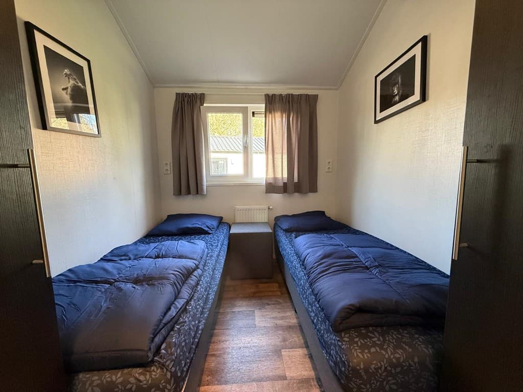 Slaapkamer met twee aparte bedden, een raam met gordijnen en enkele fotolijsten aan de muur