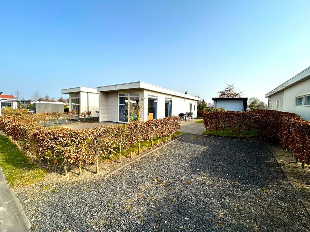 Moderne woning met grote ramen, omgeven door een lage haag en een gravelpad in een groene omgeving