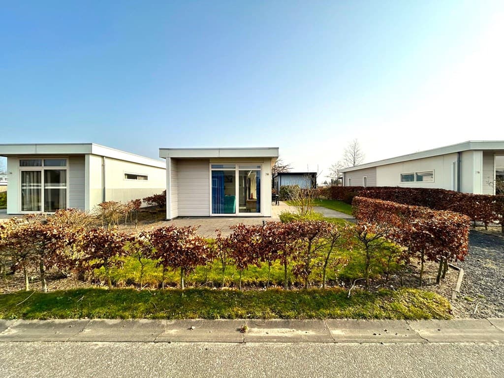 Moderne vakantiewoning omringd door groene begroeiing en een aangelegde tuin met hagen.