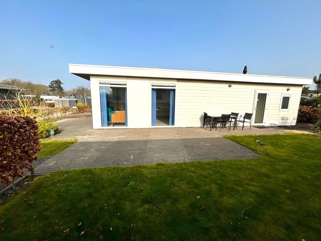 Moderne vakantiewoning met een groene tuin, stenen terras en glazen deuren die naar buiten leiden.