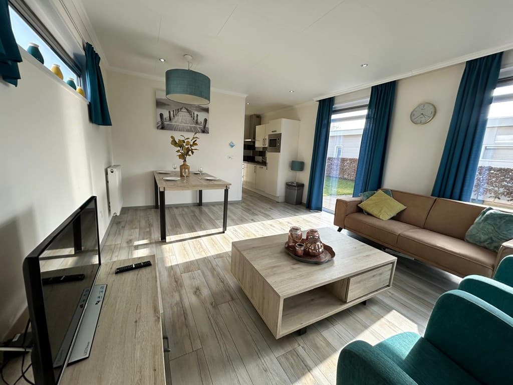 Moderne woonkamer met bank, salontafel en eettafel, uitzicht op keuken en naar buiten door grote ramen.