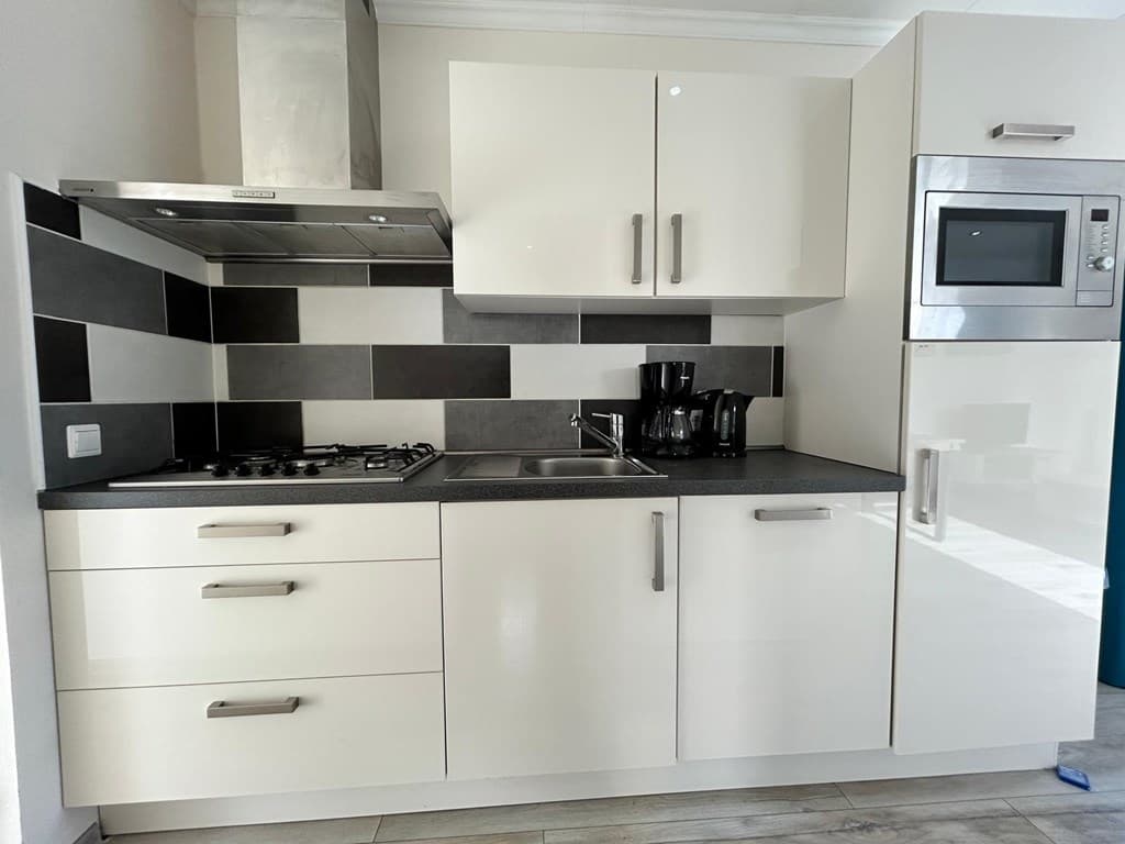 Moderne keuken met witte meubels, gasfornuis, spoelbak en ingebouwde oven en koelkast met zwarte accenten.