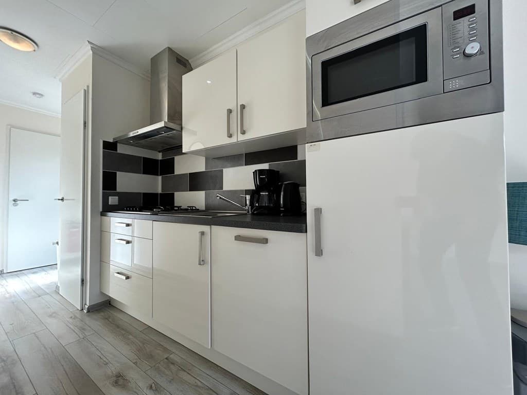 Moderne keuken met witte kasten, zwart-witte tegels, oven, magnetron en koffiezetapparaat.