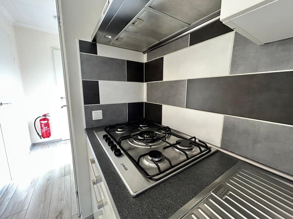 Keuken met gasfornuis en zwart-witte wandtegels, afzuigkap en spoelbak zichtbaar.