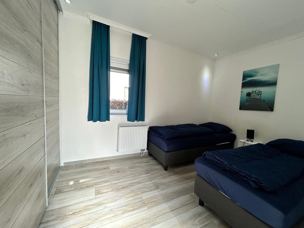 Slaapkamer met twee eenpersoonsbedden, houten vloer en raam met blauwe gordijnen.