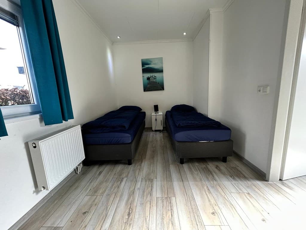 Kamer met twee eenpersoonsbedden, moderne vloer en een raam met blauwe gordijnen.