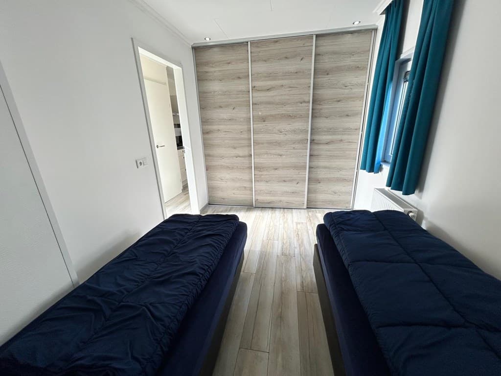 Slaapkamer met twee eenpersoonsbedden, kledingkast met schuifdeuren en een raam met blauwe gordijnen.