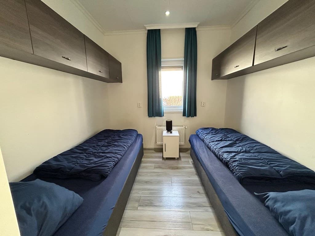 Slaapkamer met twee eenpersoonsbedden, muurkasten boven de bedden en een klein nachtkastje tussen de bedden.