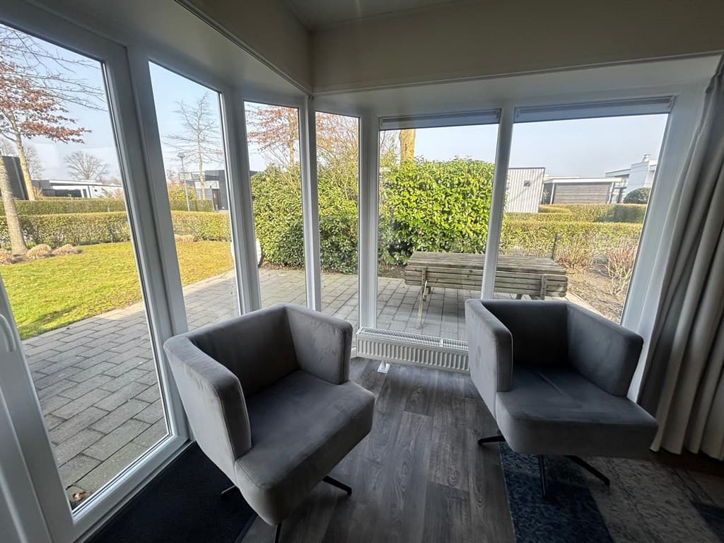 Zitruimte met twee grijze stoelen en uitzicht op een betegelde tuin met bank en groenstrook