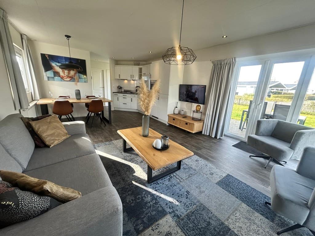 Hedendaagse woonkamer met grijze bank, houten tafel en open keuken, grote ramen met uitzicht op het buitengebied.