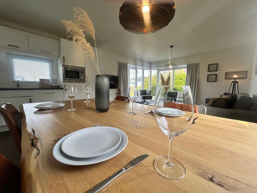Eettafel met borden en glazen, uitzicht op woonkamer met bank, raam en moderne inrichting in vakantiehuis.