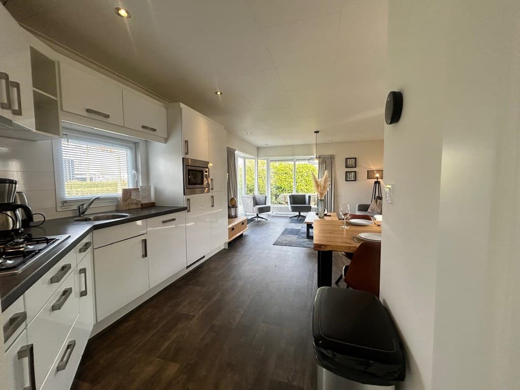 Moderne open keuken met eethoek en woonkamer met grote ramen en toegang tot de tuin.