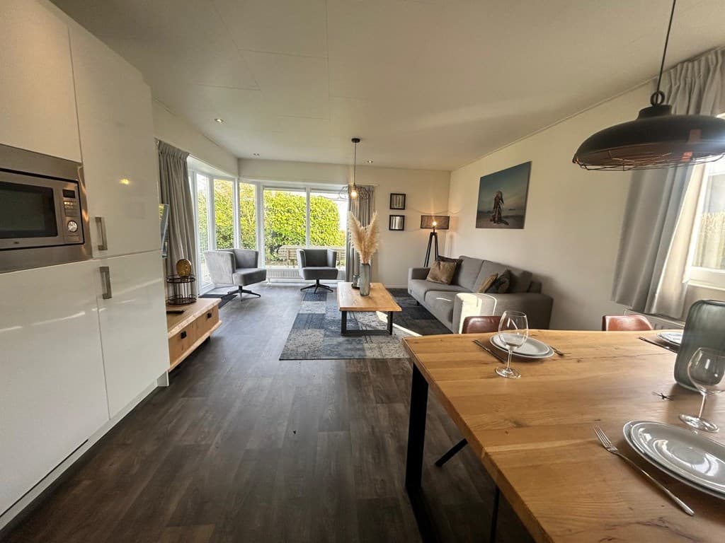 Moderne woonkamer met zithoek, eettafel en grote raampartij voor natuurlijk licht.