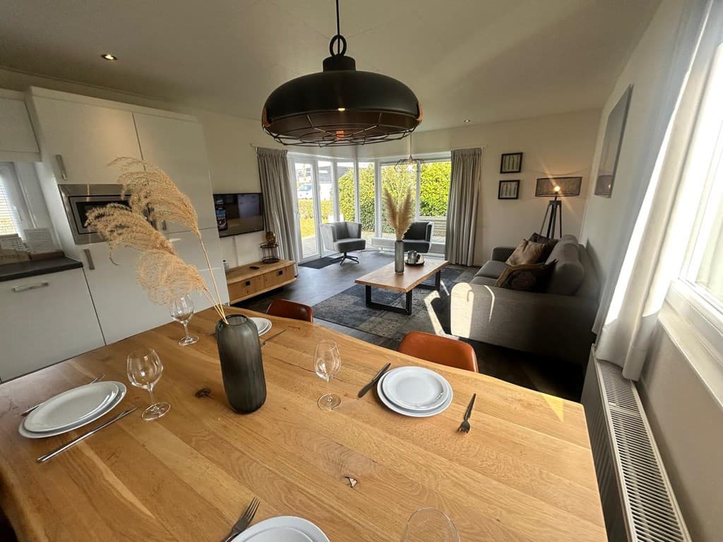 Modern interieur van een vakantiewoning met eetkamer en zithoek, grote ramen met uitzicht op de tuin.