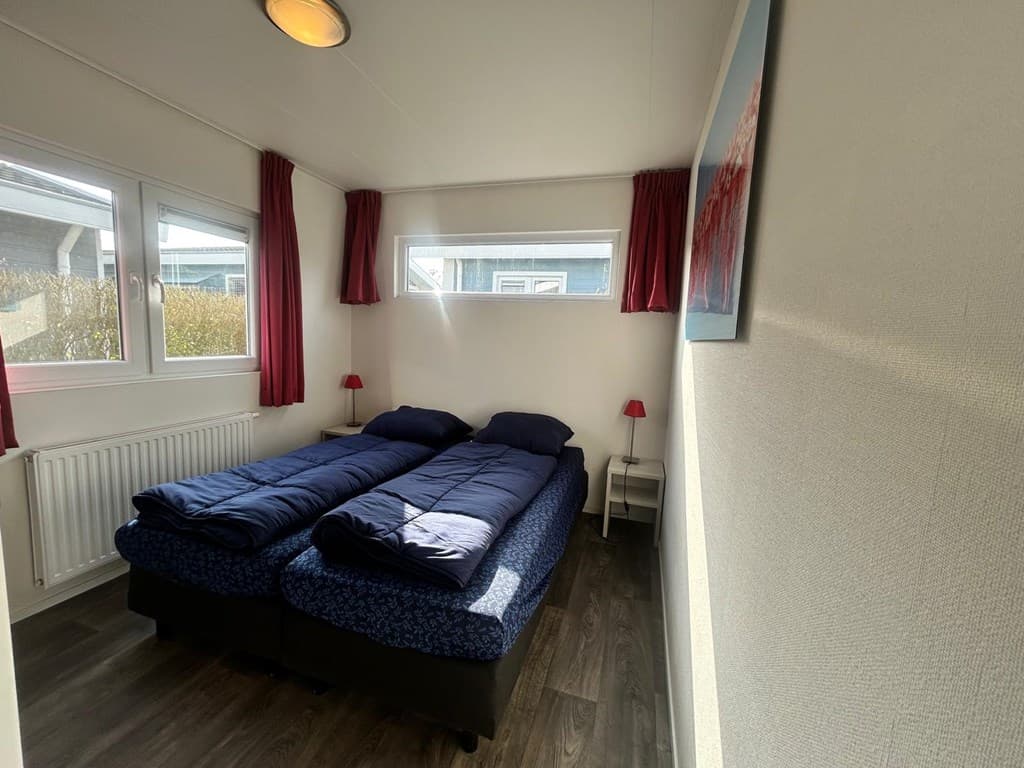 Slaapkamer met twee enkele bedden, ramen met natuurlijk licht en rode gordijnen.