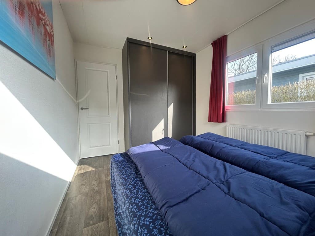 Slaapkamer met twee eenpersoonsbedden, vloerbedekking en inbouwkast, grote ramen met uitzicht op buitenlicht.