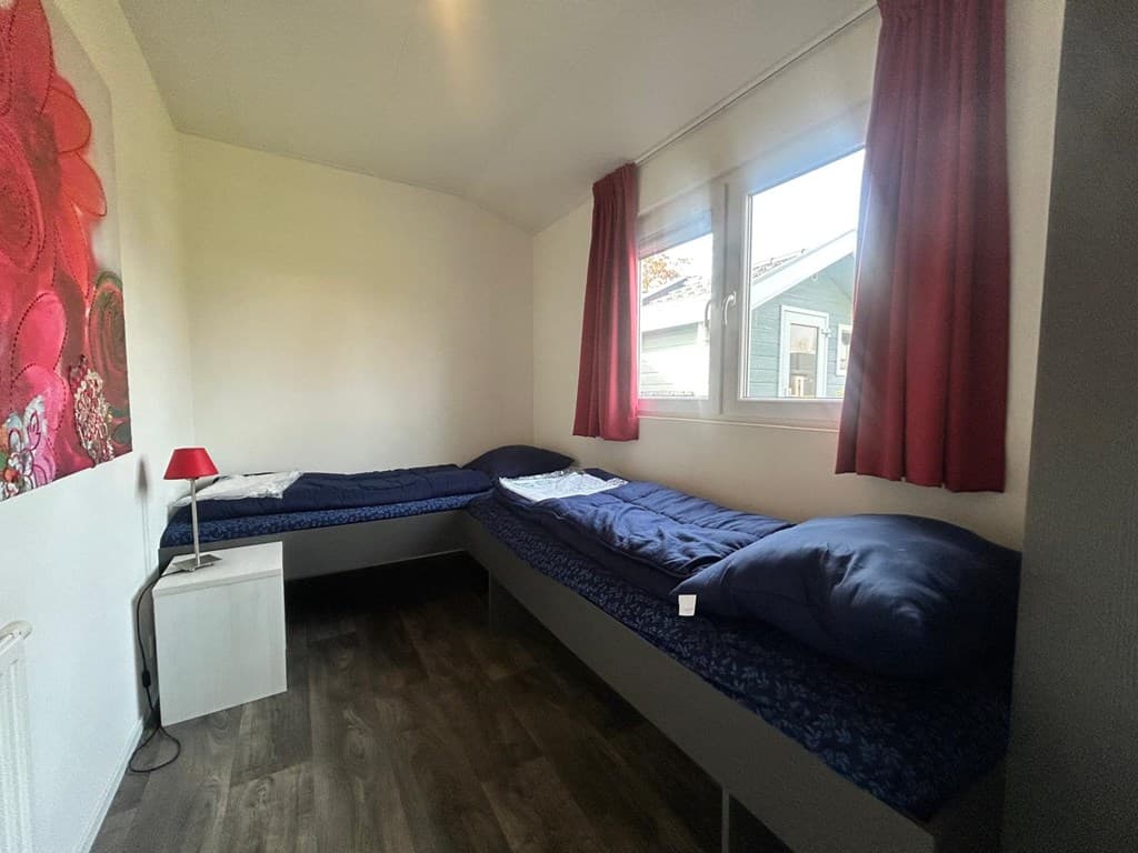 Slaapkamer met twee eenpersoonsbedden, nachtkastje, rode lamp en ramen met zicht op de buitenruimte