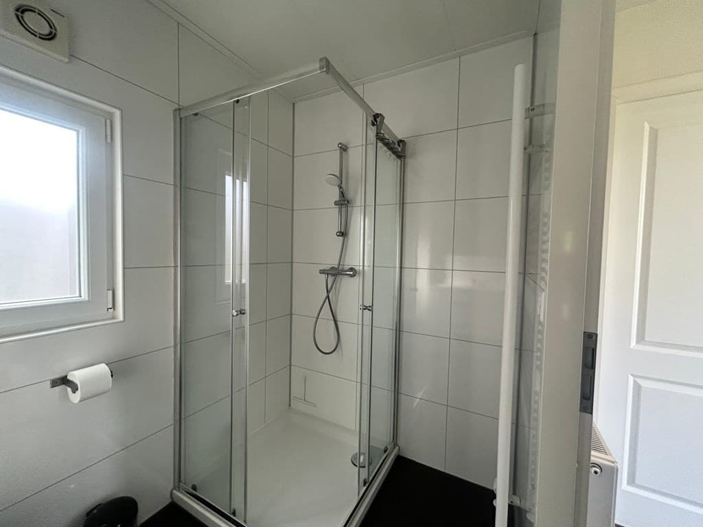 Moderne douchecabine met glazen wanden, witte tegels en een douchekop in een lichte badkamer