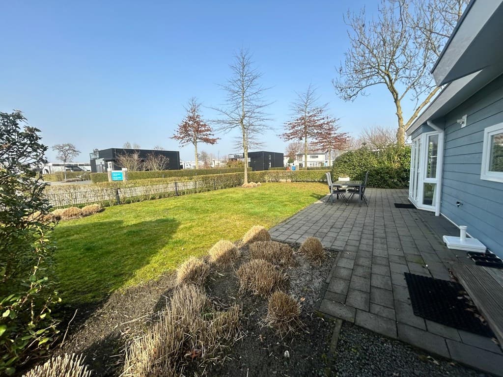 Tuin met gras en grindpad, gelegen bij een blauwe woning, gedeeltelijk zicht op moderne gebouwen en bomen in de omgeving