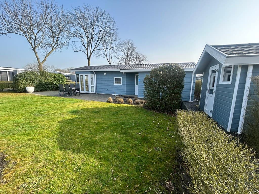 Blauw houten vakantiehuis met tuin en terras, omringd door struiken en bomen, bij EuroParcs Bad Hulckesteijn in Nijkerk.