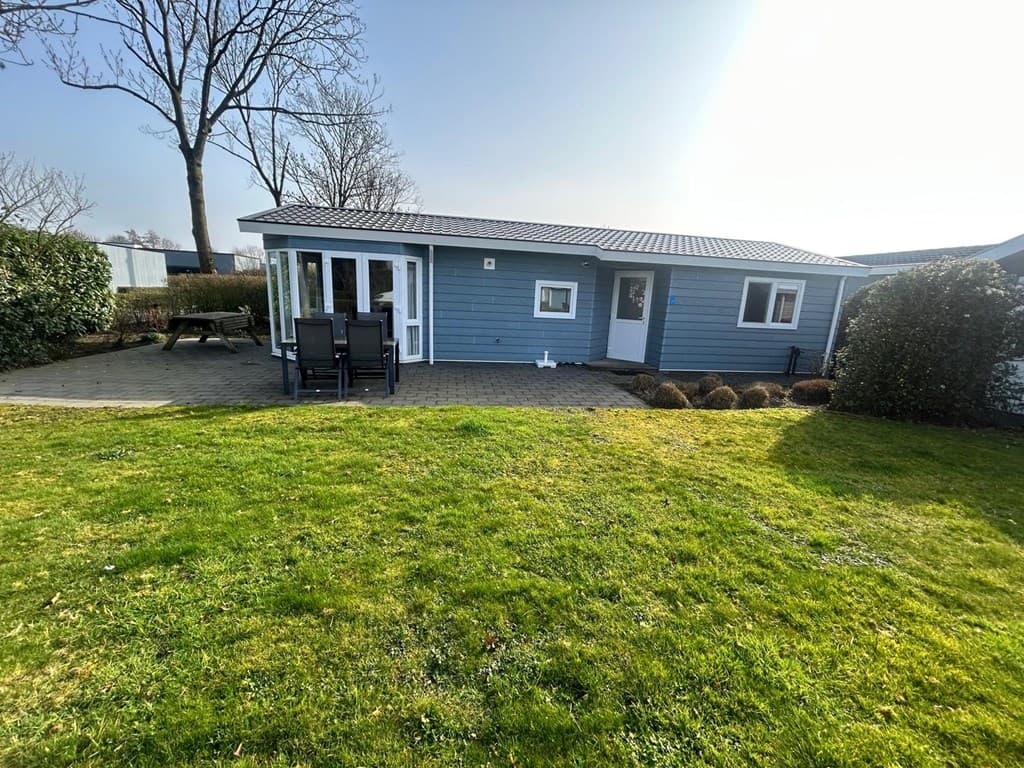 Buitenzijde van een chalet met een terras en zwarte tuinmeubelen, omgeven door gras en struiken