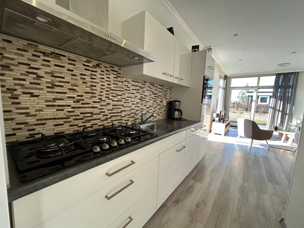 Moderne keuken met gasfornuis, chique achterwand en zicht op de woonkamer met grote ramen en natuurlijk licht